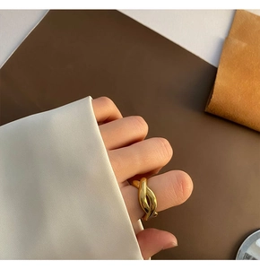 Detail of 18K gold plated twisted knot ring worn against a white shirt sleeve