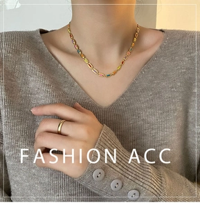 Detail of colorful enamel block necklace with gold chain on model wearing grey knitwear