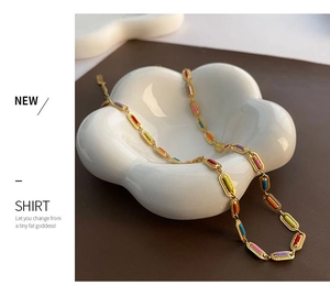 Detail of colorful enamel segments on golden stainless steel link necklace in a ceramic tray