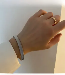 Detail of silver textured bangle and gold minimalist ring on model wrist