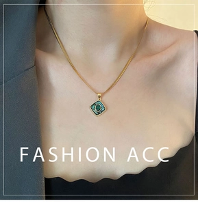 Close-up of a square abalone shell pendant on a gold snake chain worn over a grey blazer