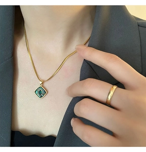 Close-up of a gold necklace with a green abalone shell pendant on a grey suit jacket
