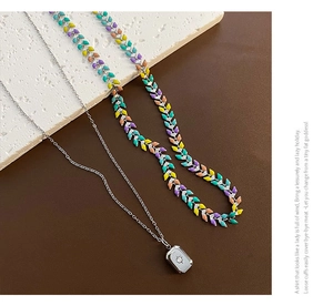Détail de colliers superposés en acier titane avec chaîne flèche colorée et pendentif zircon