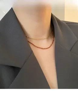 Detail of layered gold twist chain and reddish brown faceted garnet bead necklace on model