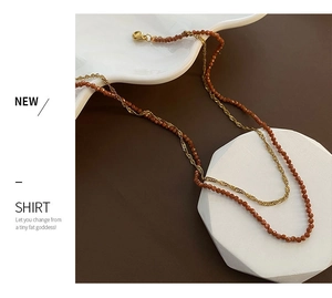 Detail showing dual-layer necklace with golden twisted chain and faceted brown gemstone beads