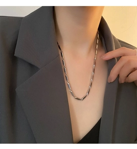Close-up of a polished silver titanium steel geometric link necklace on a grey blazer