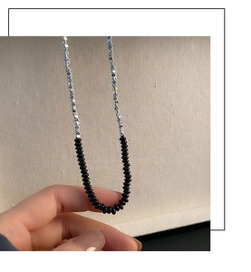 Dettaglio ravvicinato della collana di perline nere e argento su un cartoncino materico
