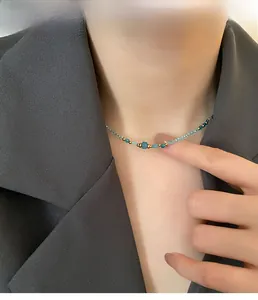 Détail d'un collier de perles bleues avec accents dorés porté sur une veste grise