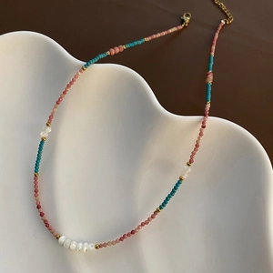 Elegant natural stone and pearl beaded necklace with gold accents on a white textured dish