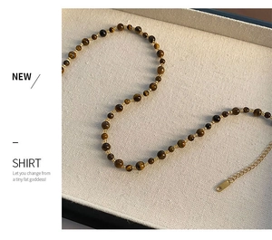 Detailed shot of tiger eye beaded necklace with gold adjustable chain on fabric tray