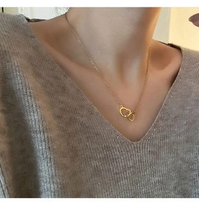 Close-up of interlocking gold heart pendants on a fine chain worn with a knit sweater