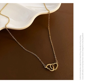 Macro detail of intertwined double heart pendant necklace in polished golden finish