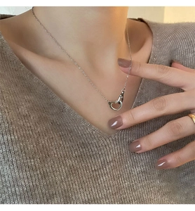Close-up of a silver intertwined heart pendant necklace worn on a brown knit sweater
