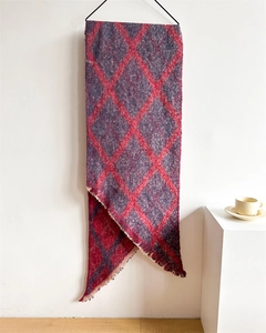 Détail d'une écharpe en maille épaisse avec motif à losanges rouges et franges sur fond sobre