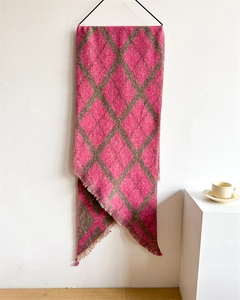 Détail d'une écharpe à carreaux rose et marron avec des bords à franges sur un mur
