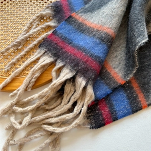 Close-up of thick striped winter scarf with plush fringe tassels on vintage woven tray