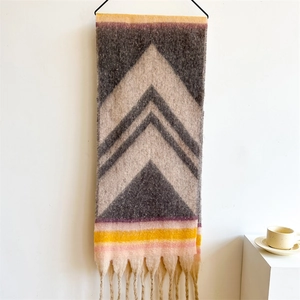 Detail of multi-color geometric knit scarf with long handmade tassels on white wall