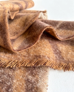 Détail macro du tissu d'une écharpe à carreaux aux tons caramel et bords à franges
