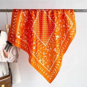 Close-up of orange silk scarf with white floral and polka dot patterns on metal hanger