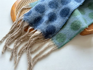 Close-up of thick knitted wool-like scarf featuring polka dots and long fringe tassels