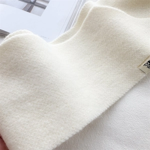Close-up of soft beige knitted scarf texture with minimalist logo label and fuzzy surface
