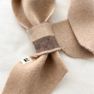 Detail of soft ribbed knit scarf in camel with cross-over design and logo tag