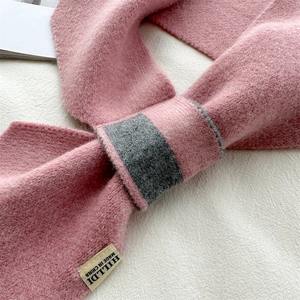 Close-up of soft pink knitted scarf with gray contrast detail and brand label texture