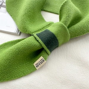 Close-up of bright green knitted scarf with textured wool fabric and sewn brand label