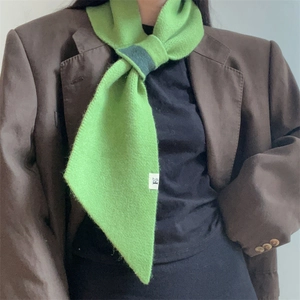 Detail of green knitted scarf with cross-loop design and stylish woven label detail
