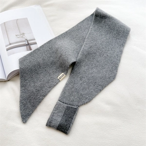 Detail of grey knitted scarf with contrast trim and logo label on fabric background