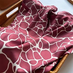 Détail d'un foulard effet soie avec motif girafe bordeaux et blanc dans un panier en osier