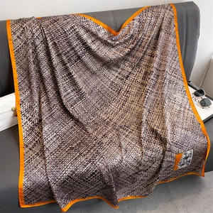 Detail of a large silk square scarf with geometric patterns and orange hem on a sofa