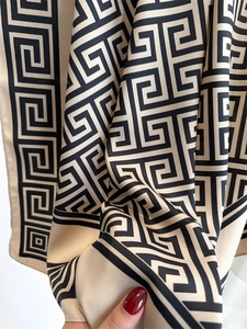 Vue détaillée d'un foulard en soie beige avec motif grec noir et texture satinée
