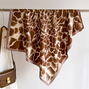 Détail d'un foulard en soie à motif girafe drapé avec un sac en cuir marron sur support