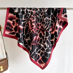Gros plan du foulard en soie à imprimé girafe et bordure rouge drapé près d'un sac en cuir