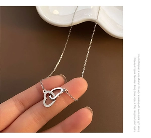Detail of silver interlocking heart necklace pendant held over a minimalist dish