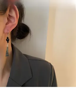 Close-up of long black teardrop earrings with silver hooks on a model in vintage style