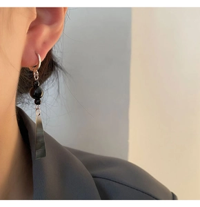 Close-up of long black beaded earrings with trapezoid pendant on a female model