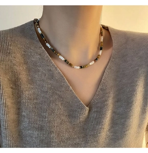 Détail d'un collier de perles naturelles colorées avec perles dorées sur pull gris