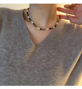 Détail du collier ras du cou en perles naturelles porté avec un pull en maille marron