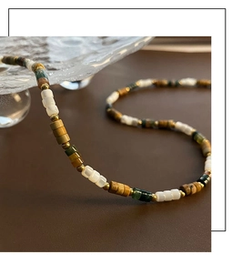 Détail du collier de perles naturelles aux tons terreux avec accents dorés sur fond brun