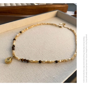 Macro detail of teardrop pendant necklace with brown beads and golden accents