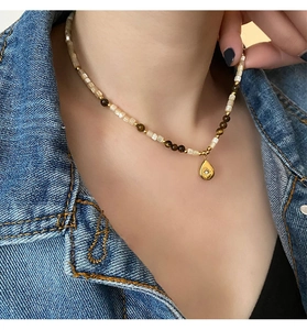 Close-up of teardrop pendant necklace with brown beads on a denim jacket background