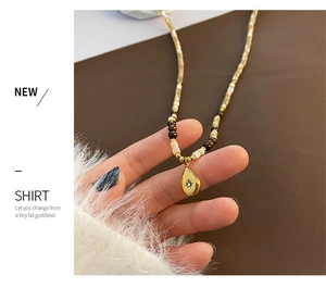 Macro detail of teardrop gold pendant with sunburst engraving and tiger eye beaded chain