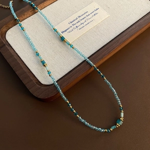 Detail of handmade beaded necklace with blue crystal beads and gold spacers in wood tray