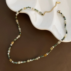 Detail of handcrafted beaded necklace with natural stones on a wavy white plate