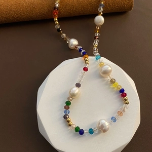 Close-up of handmade rainbow beaded necklace with natural pearls on geometric pedestal