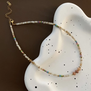 Close-up of bohemian beaded necklace with colorful stones and gold clasp on a ceramic tray