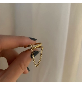 Close-up of a double-layer gold titanium ring with a fine hanging chain on beige fabric