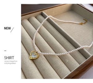 Detail of a thin pearl necklace featuring a gold-edged white heart pendant on a linen display